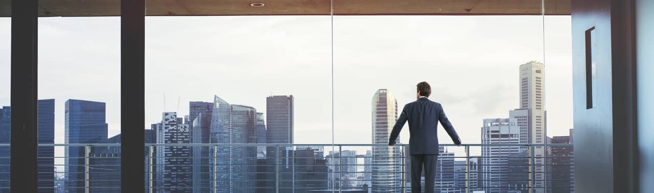 Suited man stood at a balcony overlooking a london city landscape.