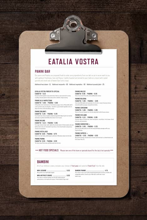 Dark wood background with a front view of a clip board holding a white sheet of paper with the menu for Eatalia Vostra.