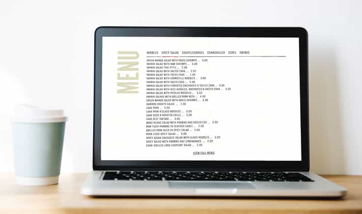 Menu section of one page website template, featuring simple text shown on a laptop computer sat on a plain wooden table top with a plain grey wall behind.