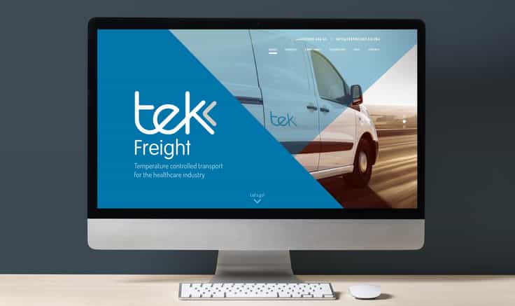 Desktop computer on light wooden desk showing Tek Freight homepage on the screen