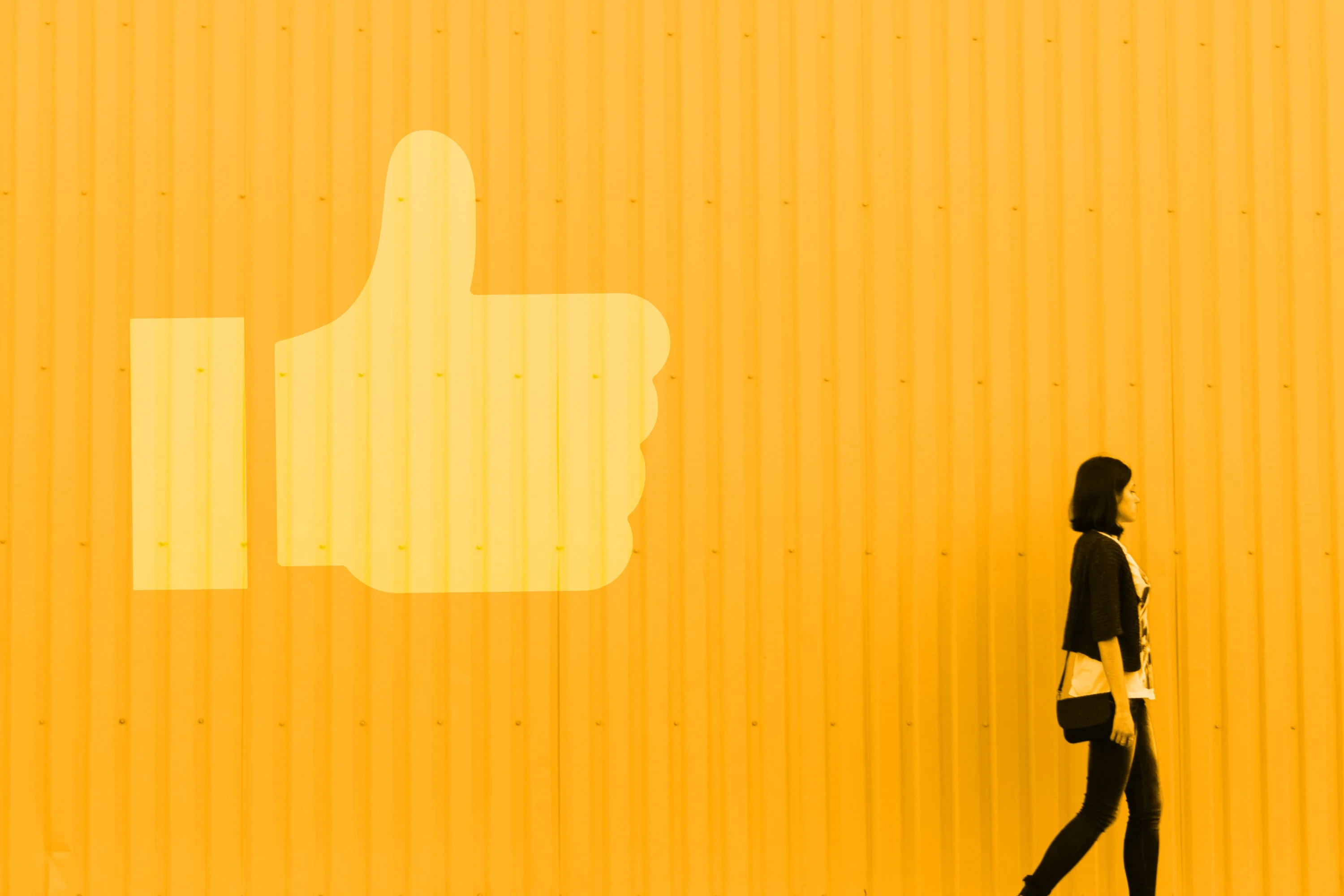 woman walking past large facebook like icon yellow wall