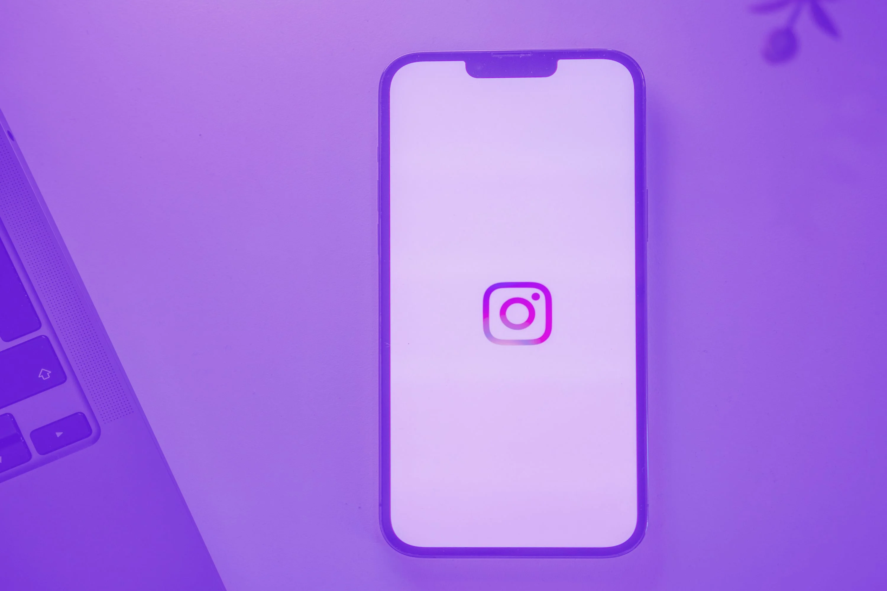 iphone showing instagram app logo next to laptop keyboard purple