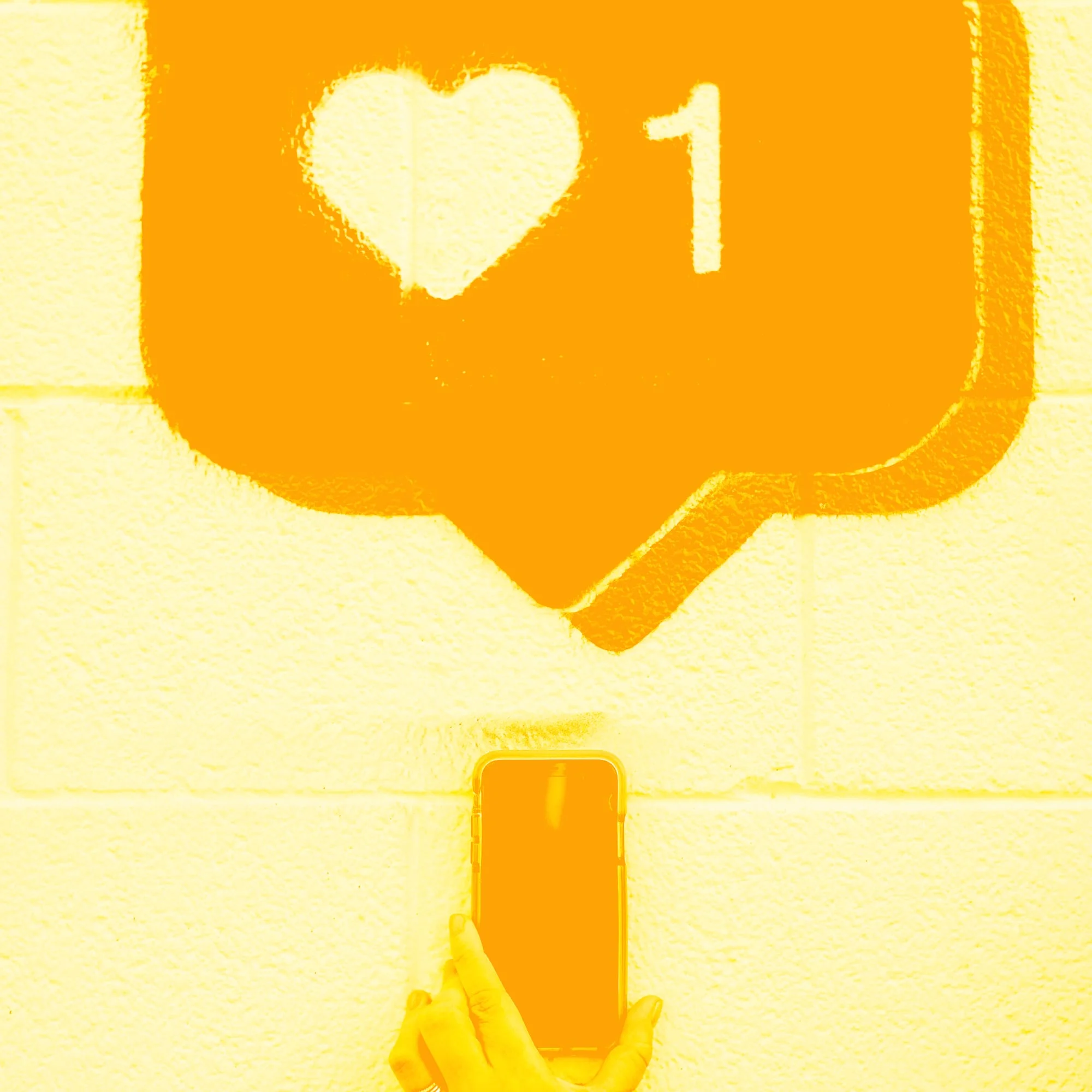 hand holding phone under instagram heart like notification brick wall golden