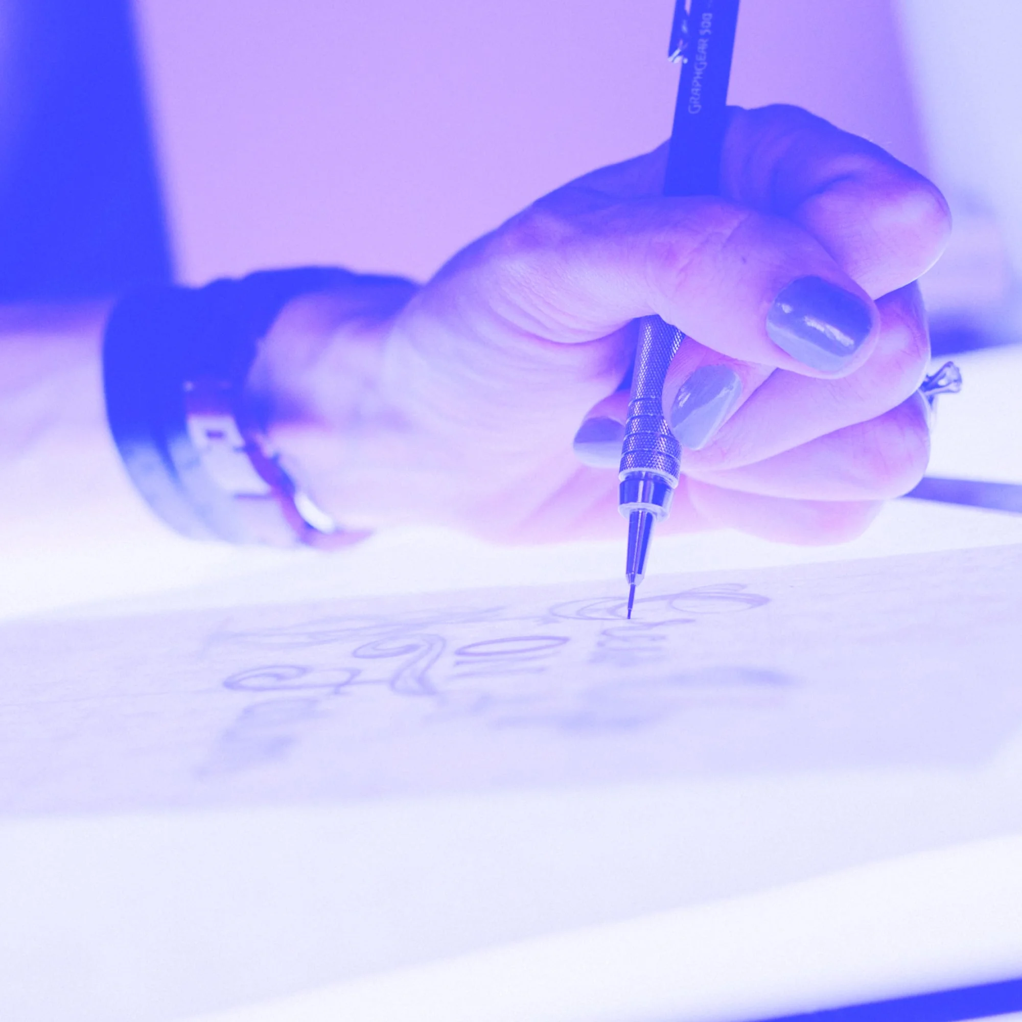 hand holding technical drawing pen sketching logo lettering on light table purple