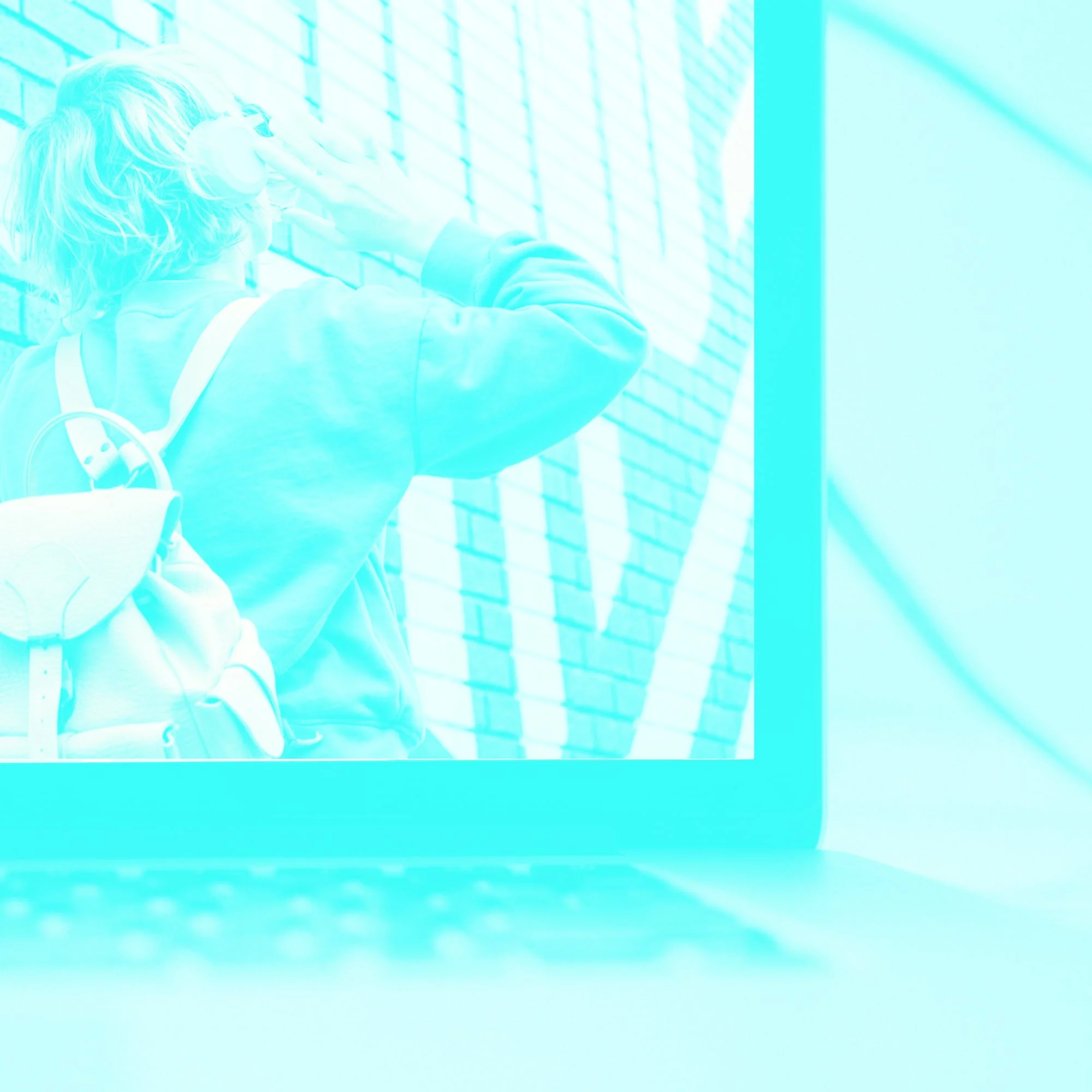 laptop screen showing woman with bag next to brick wall teal toned