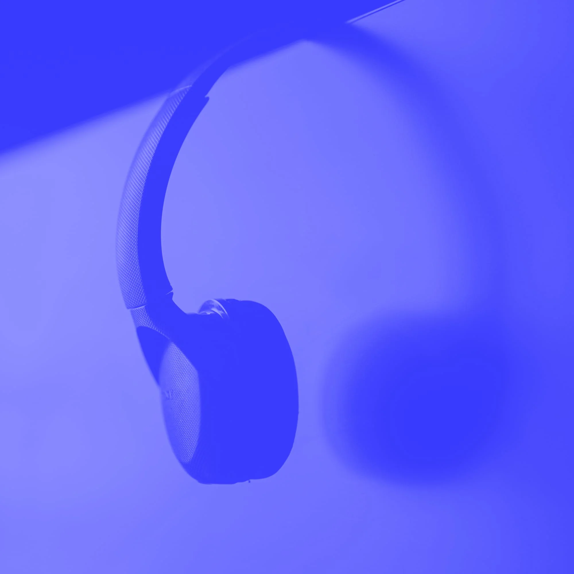 wireless over ear headphones hanging on monitor corner blue toned