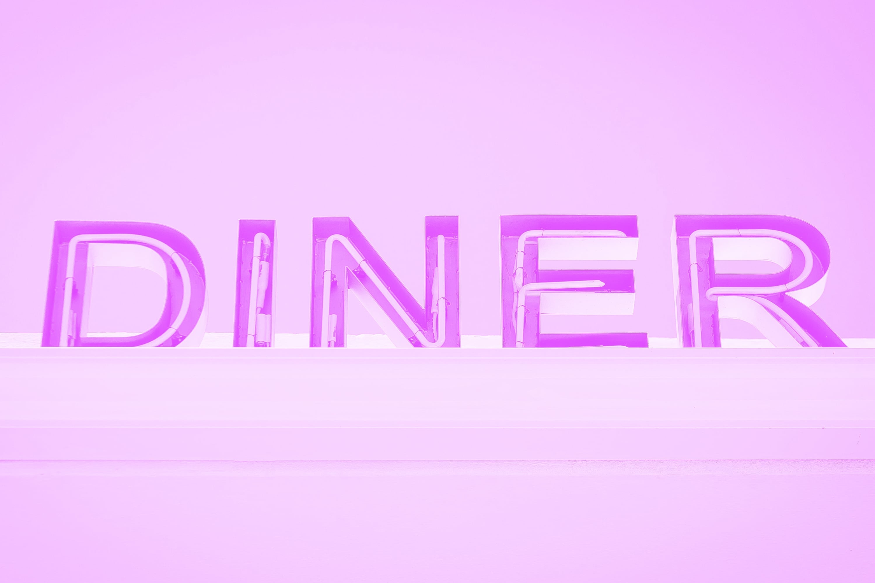 large illuminated diner neon sign letters on exterior building wall pink purple