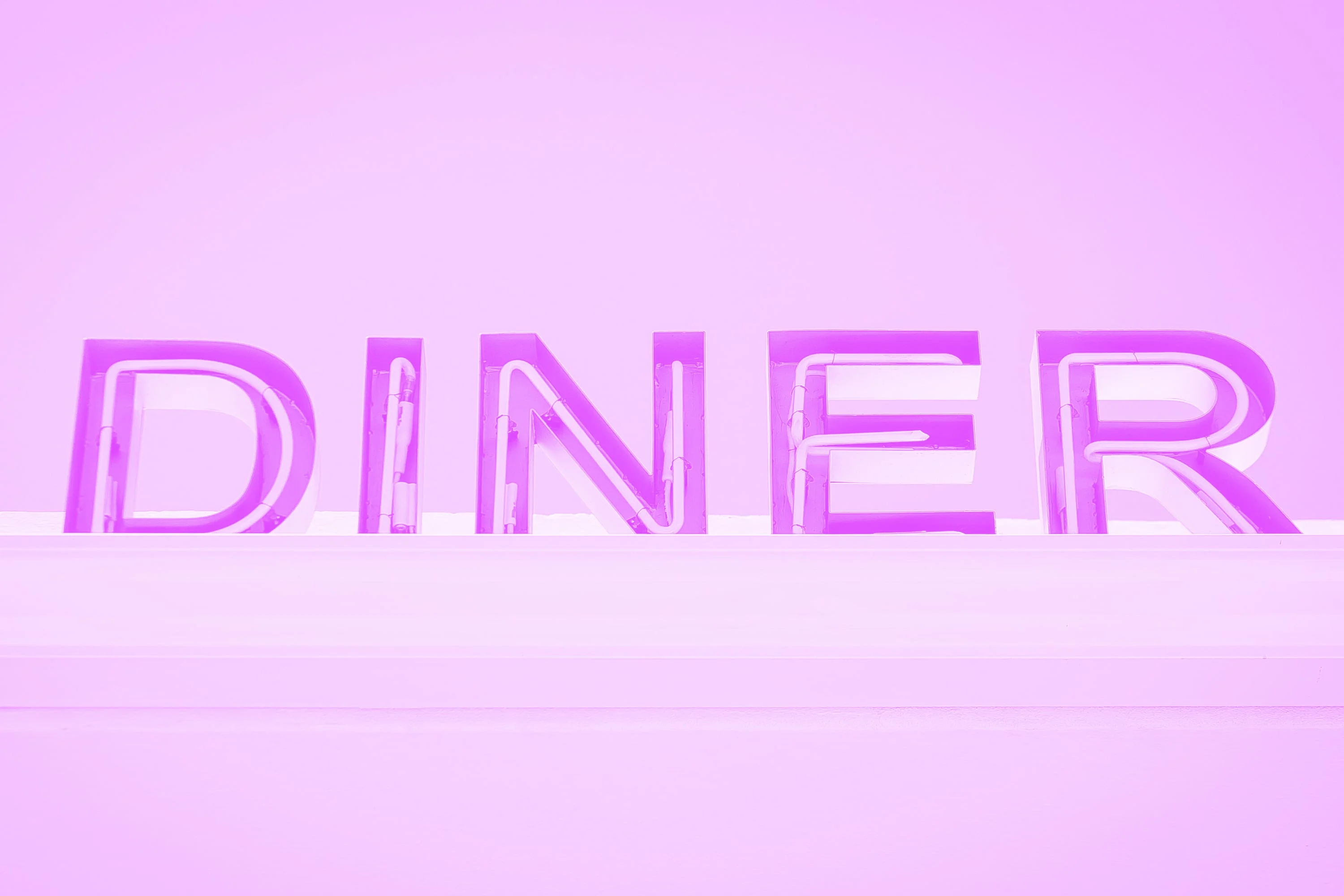 large illuminated diner neon sign letters on exterior building wall pink purple