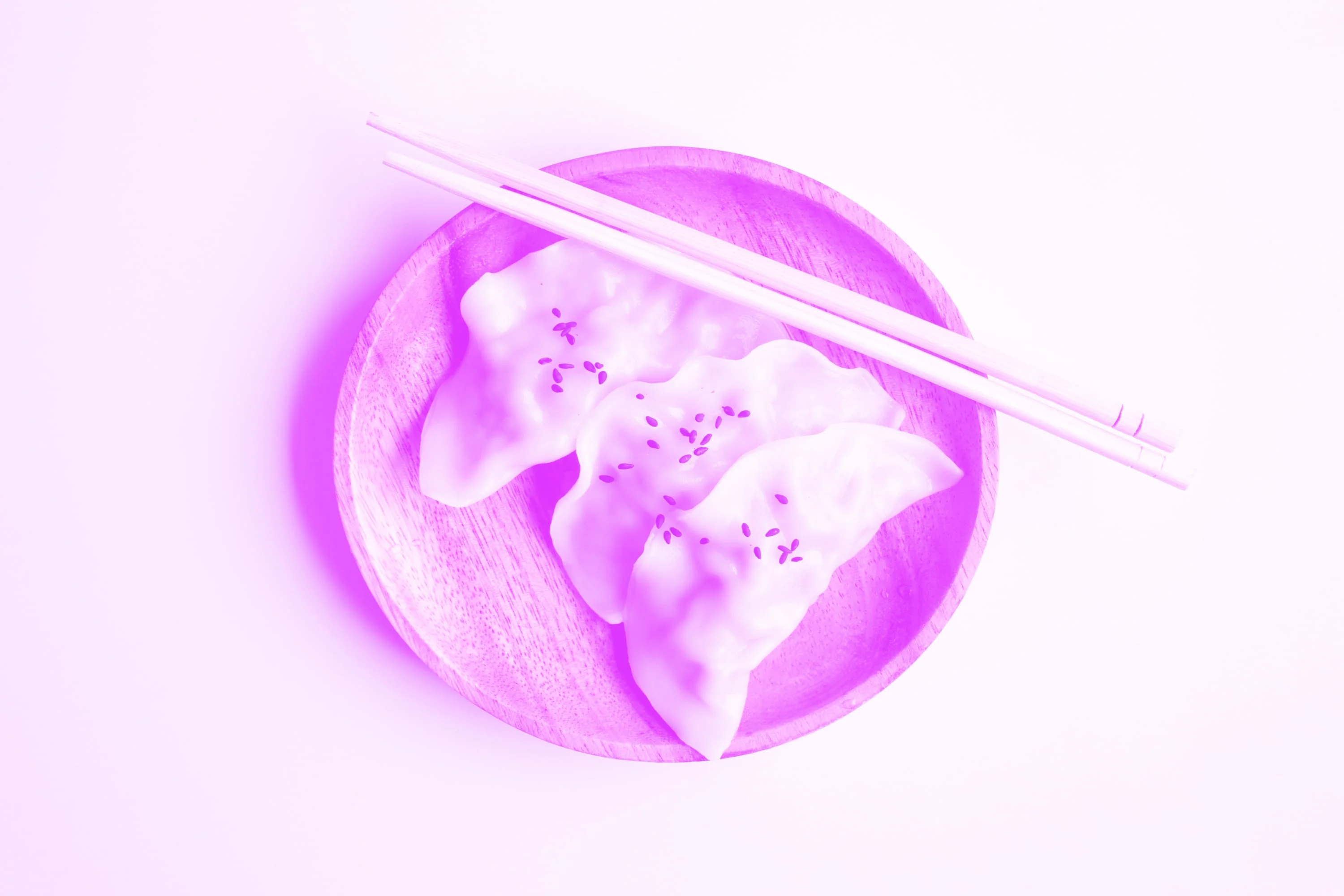 three gyoza dumplings with sesame seeds on wooden board with chopsticks pink purple