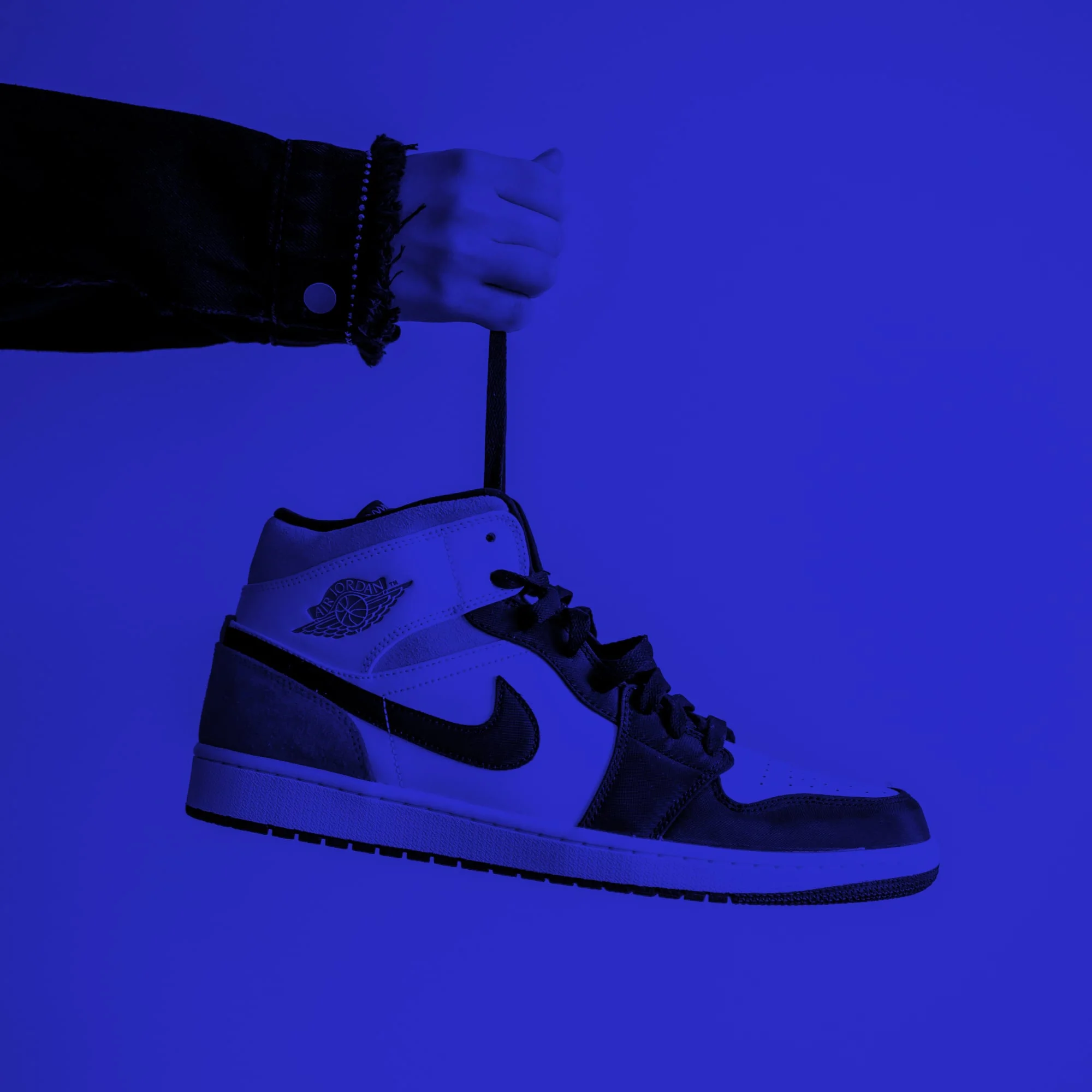 hand holding air jordan 1 sneaker by lace dangling blue toned