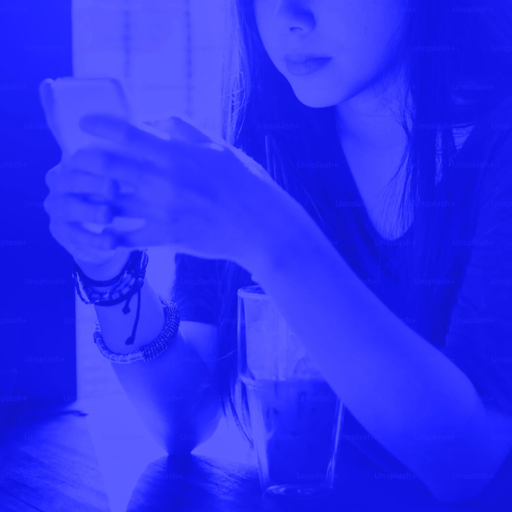 young woman with long hair holding smartphone and coffee cup blue toned