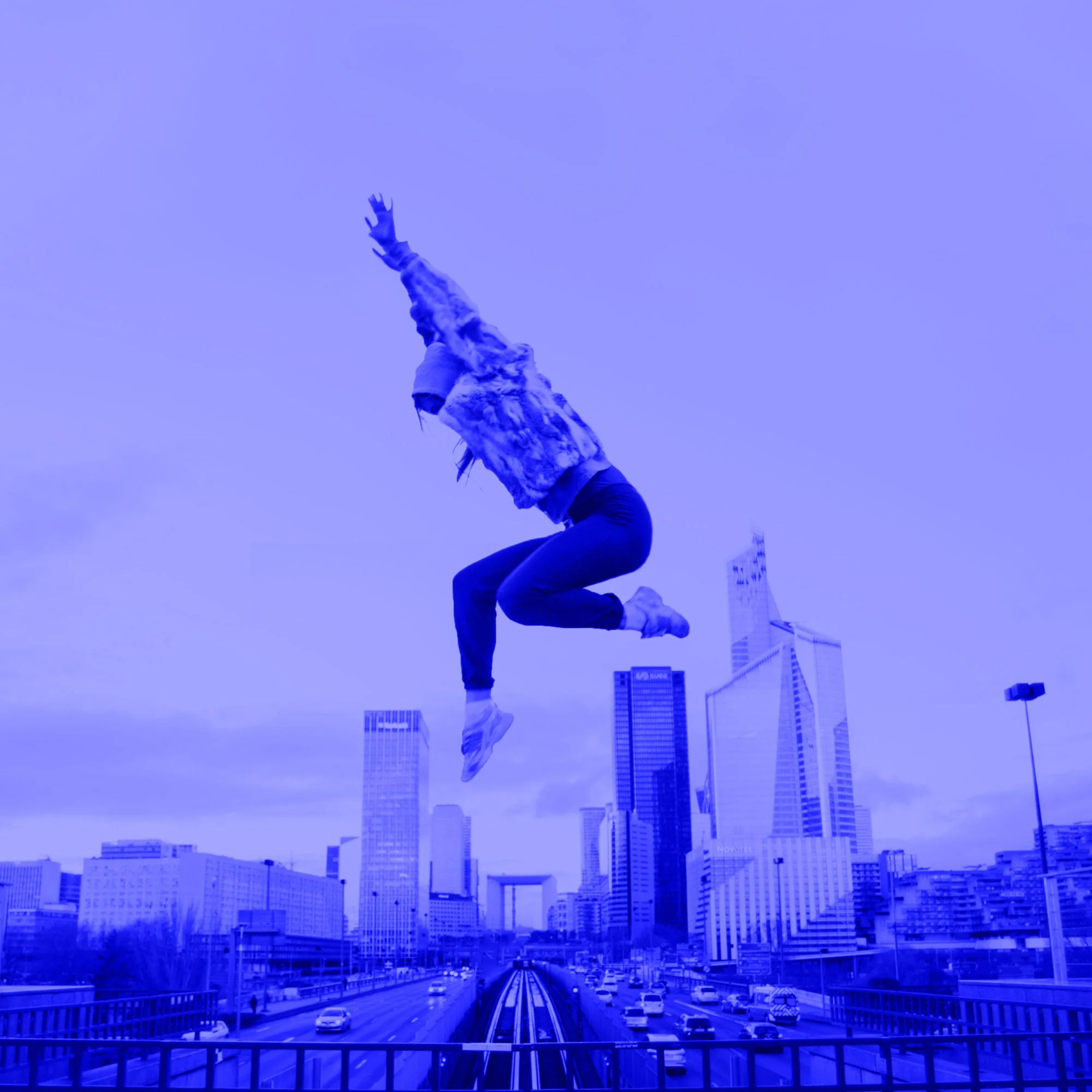 woman jumping high in mid air against city skyline with skyscrapers blue toned