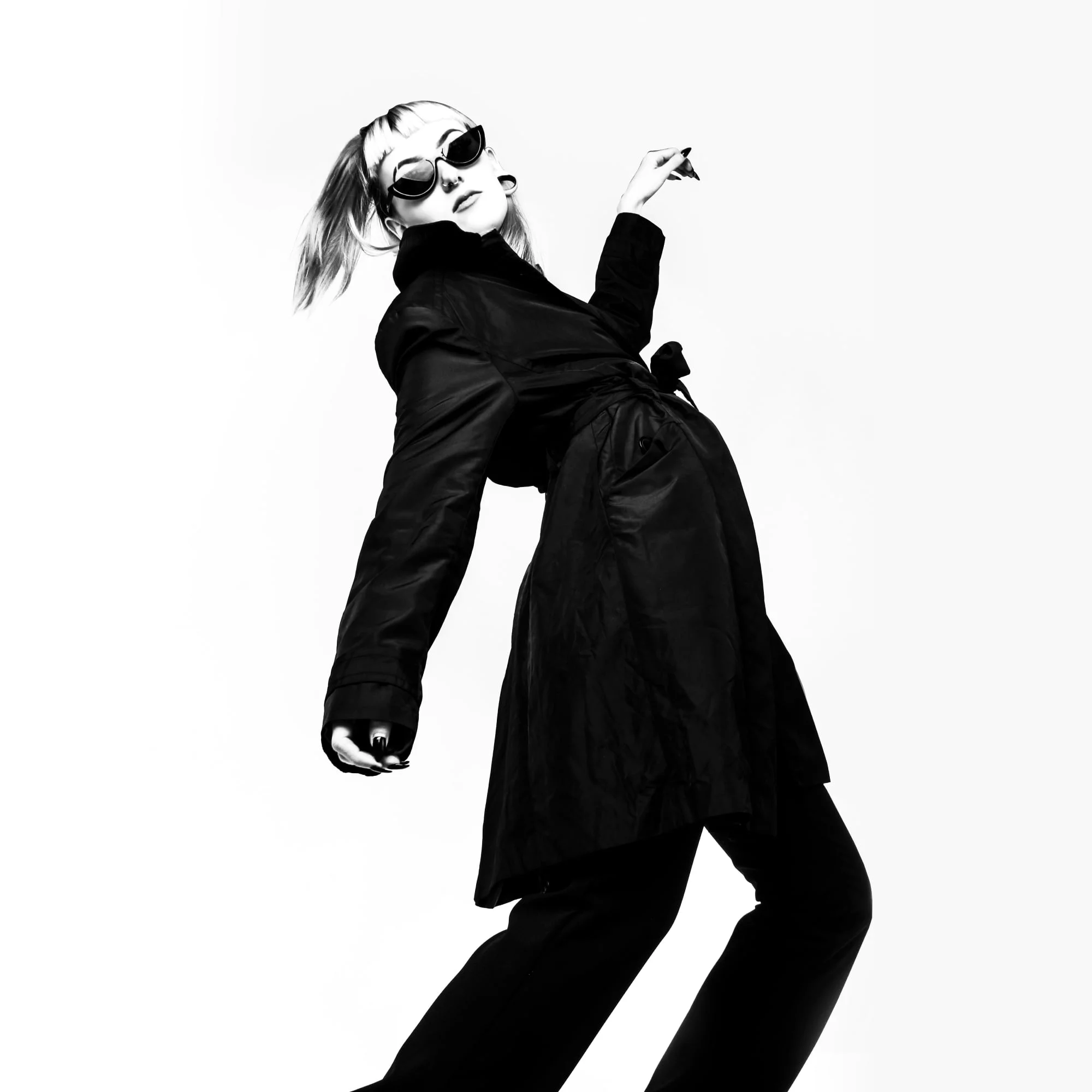 fashion model in black coat and sunglasses striking editorial pose black and white