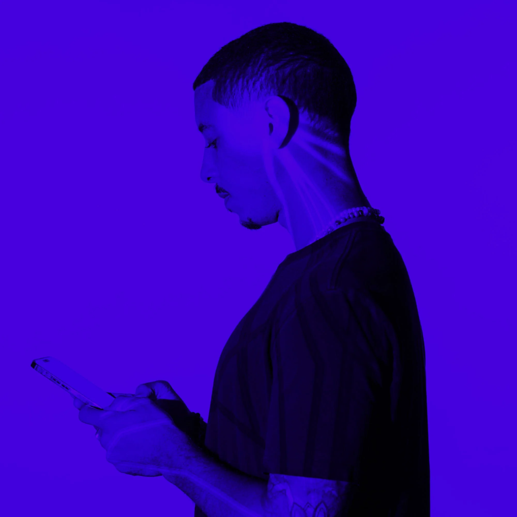 man with shaved head browsing smartphone side profile purple toned