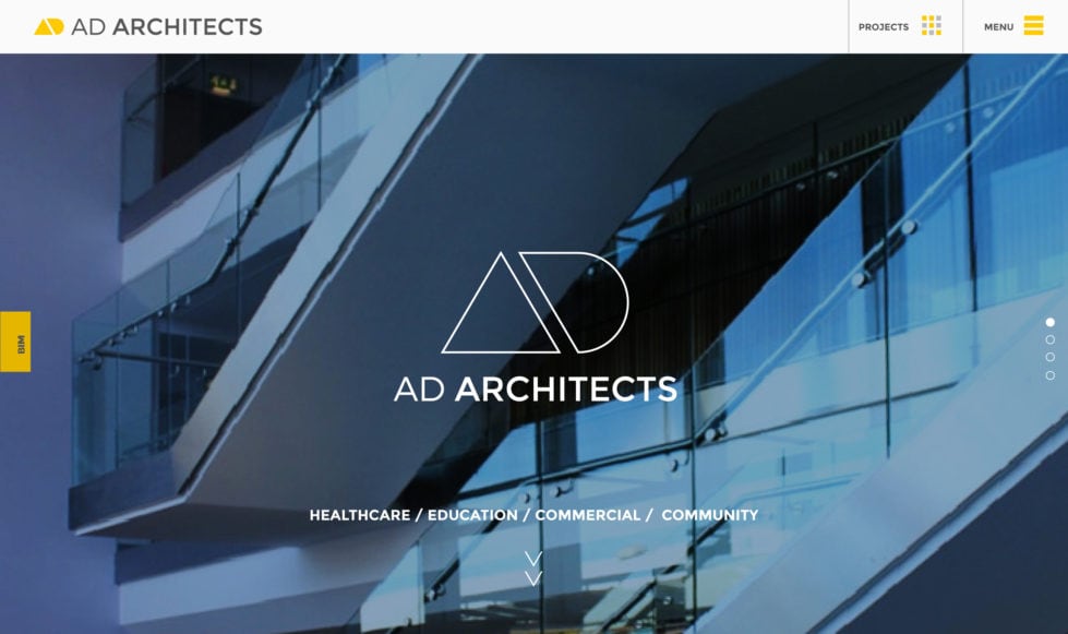 Best architecture websites AD Architects homepage hero section comprising a blue-tinted photo of a glass-fronted building with a white AD monogram and intro text reversed out white.