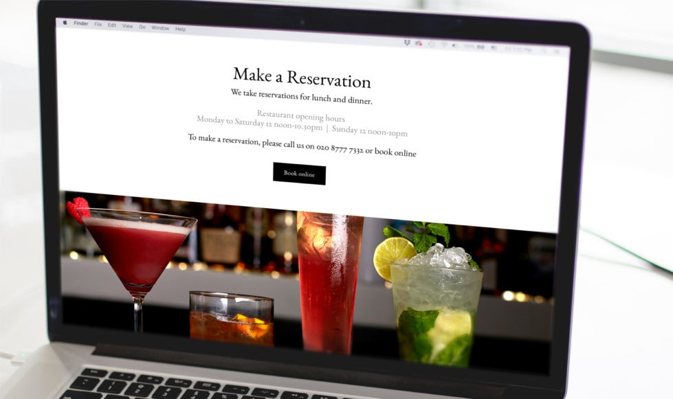 Reservations Laptop on white desktop with white background, showing reservations section from restaurant website, with close-up photograph of four cocktails in a line underneath it.