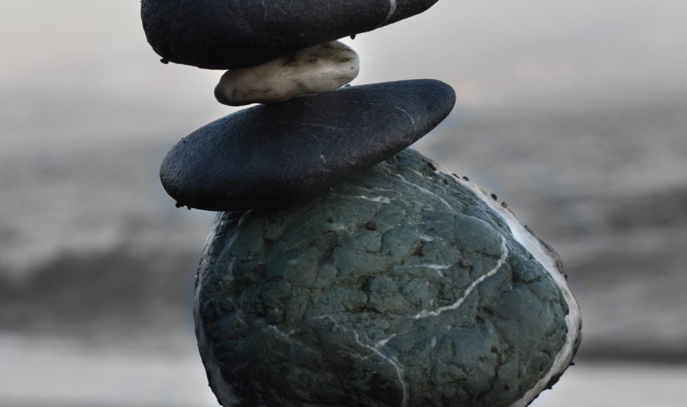 Detail Close-up image of carefully balanced pile of stones on beach with waves breaking in distance.