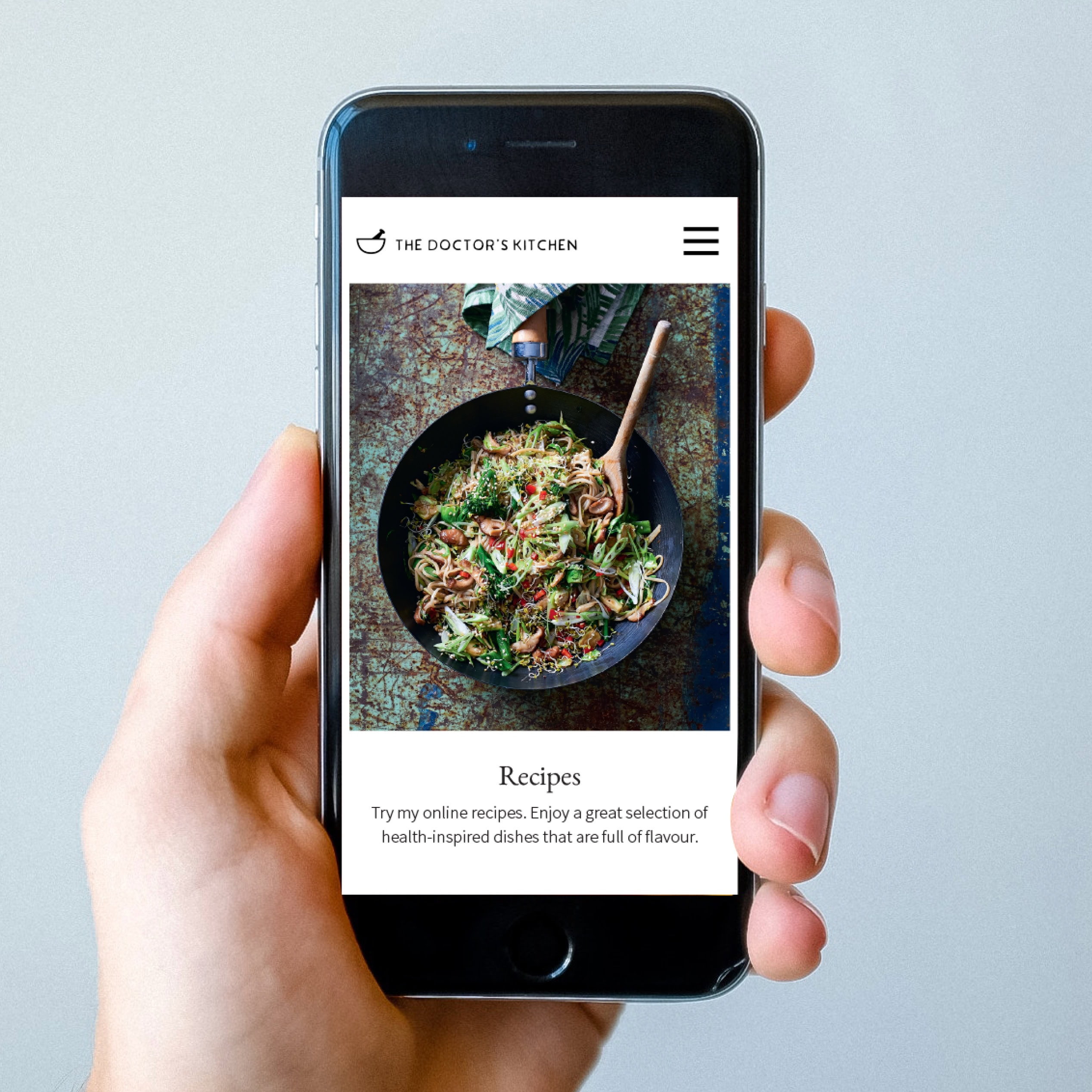 Hand holding a phone showing The Doctor’s Kitchen recipes page on mobile