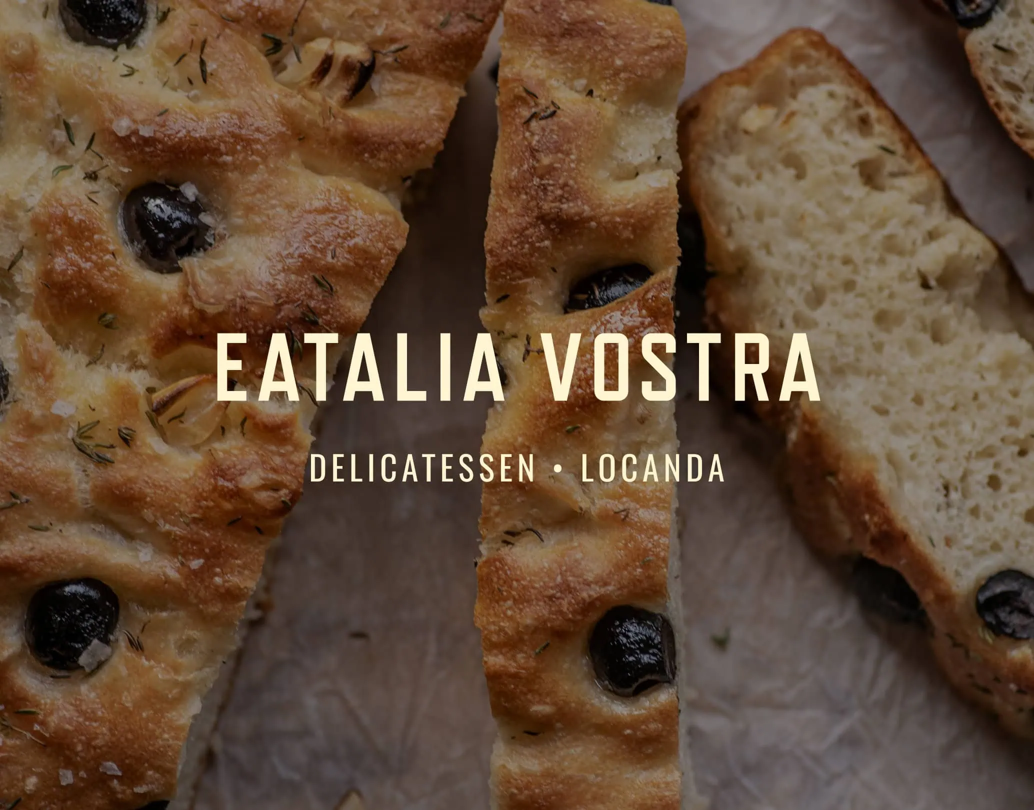 Eatalia Vostra wordmark over sliced olive focaccia sprinkled with herbs on baking paper