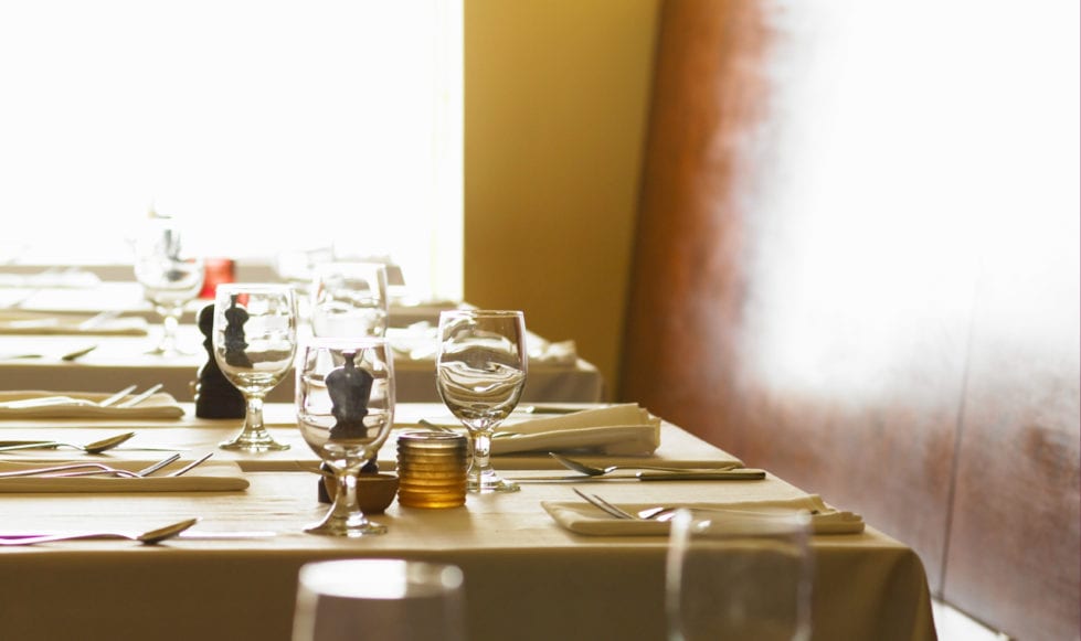 Interior shot of restaurant. Bright image shot across table with wine glasses and place settings.