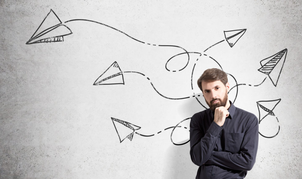 Pensive man with looping, looping paper aeroplanes on drawn on wall behind him.