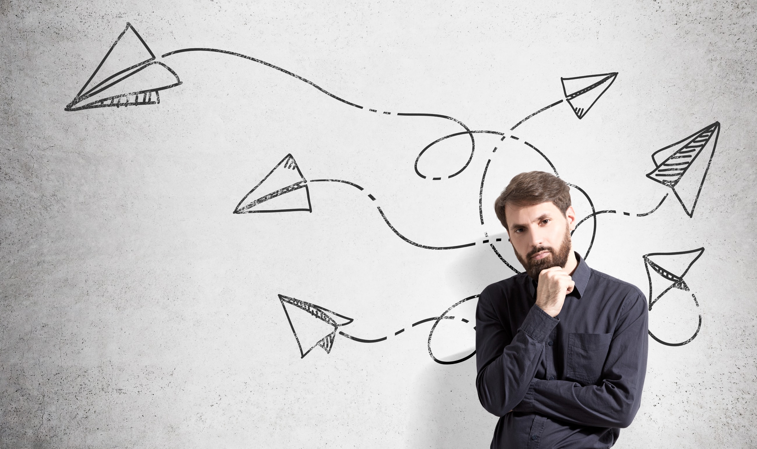 Pensive man with looping, looping paper aeroplanes on drawn on wall behind him.