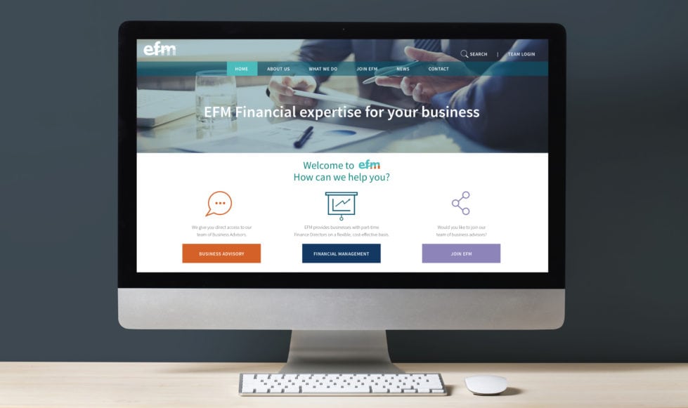 Financial website design Front on view of desktop computer screen on a light wooden worktop with a dark grey background. Screen shows the homepage top section of the EFM financial website.