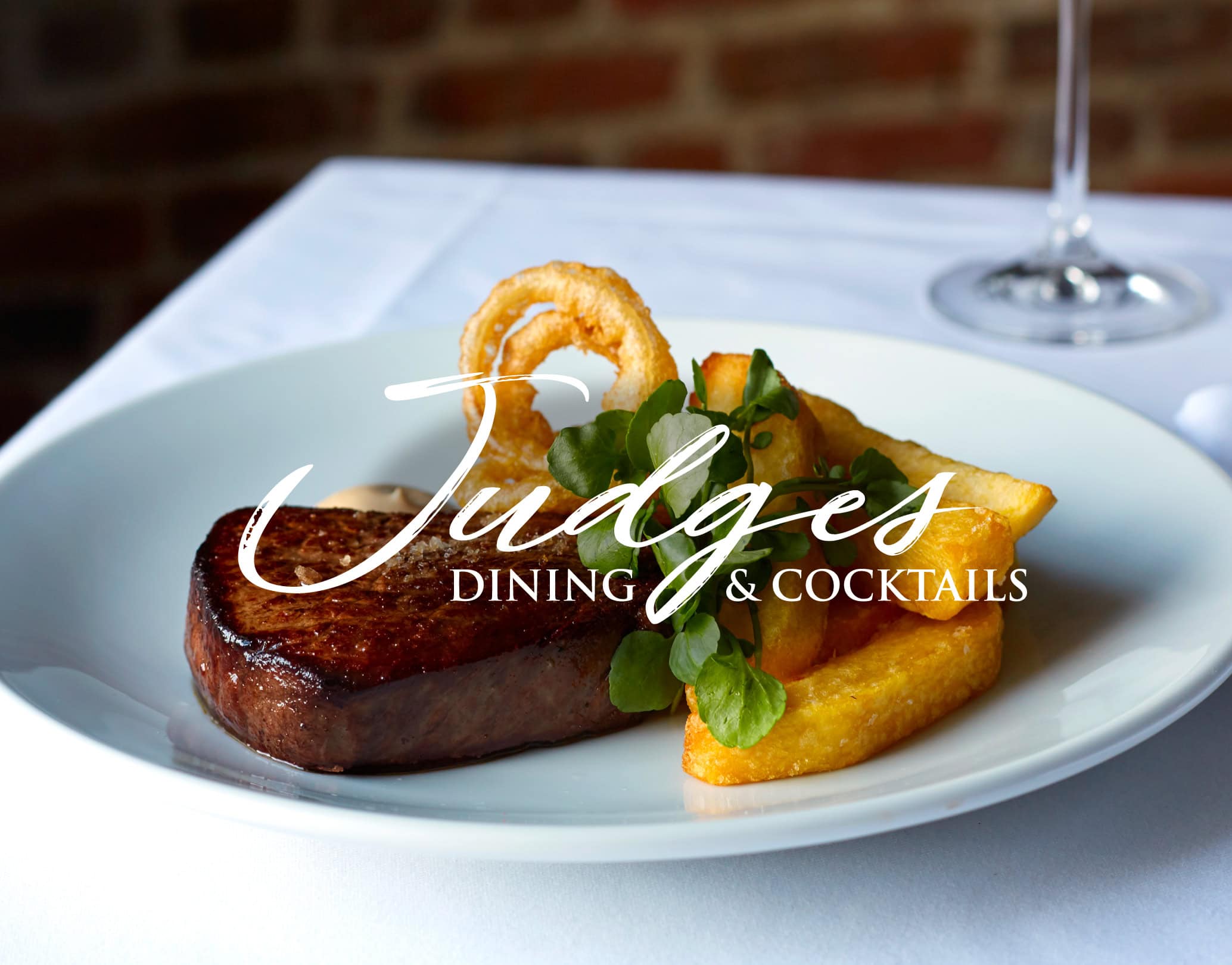 Judges Dining & Cocktails branded photo of steak with chips, onion ring and watercress on a white plate