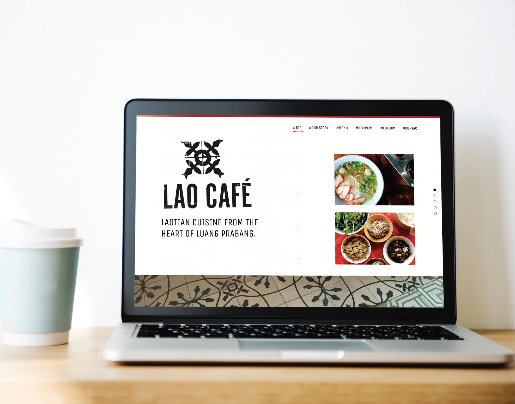 Laptop on a desk showing the Lao Café one-page website layout, with food photography panels and a takeaway coffee beside it