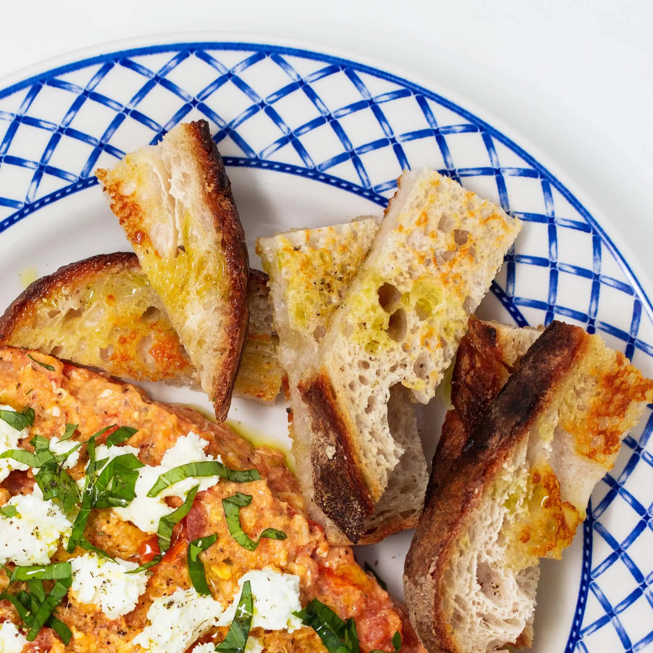 Greek dip topped with feta and herbs served with toasted bread on a blue patterned plate
