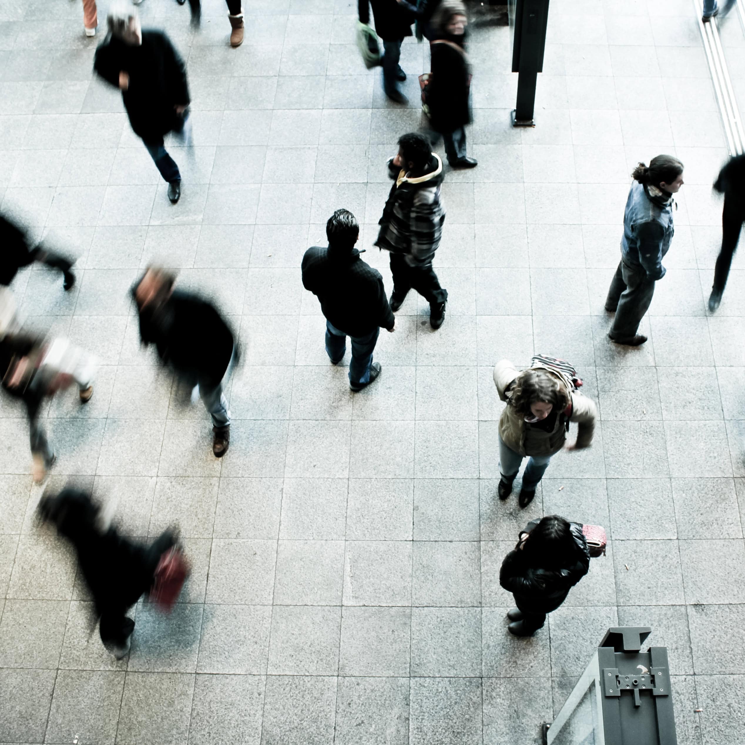 Overhead view of people walking across a tiled public concourse