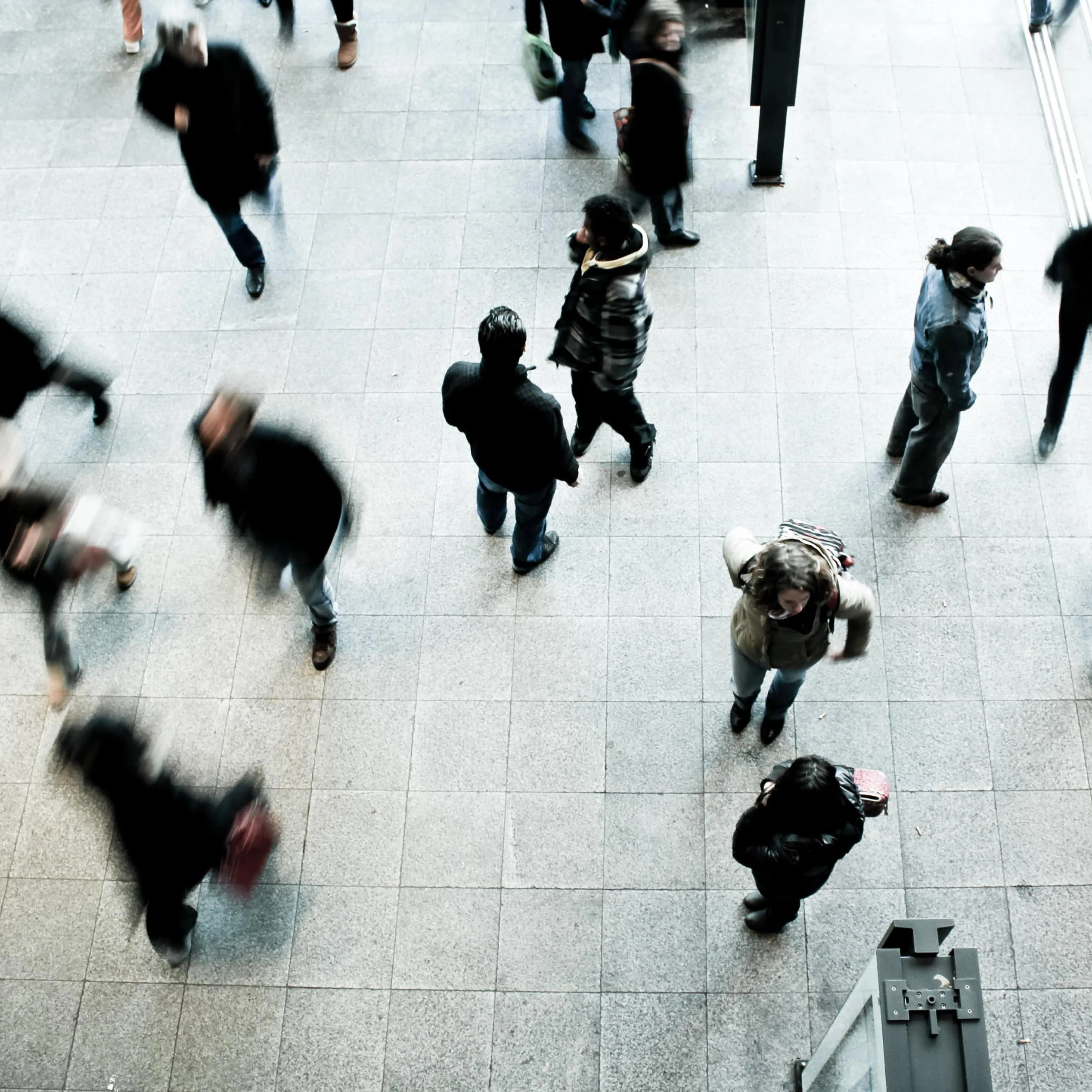 Overhead view of people walking across a tiled public concourse