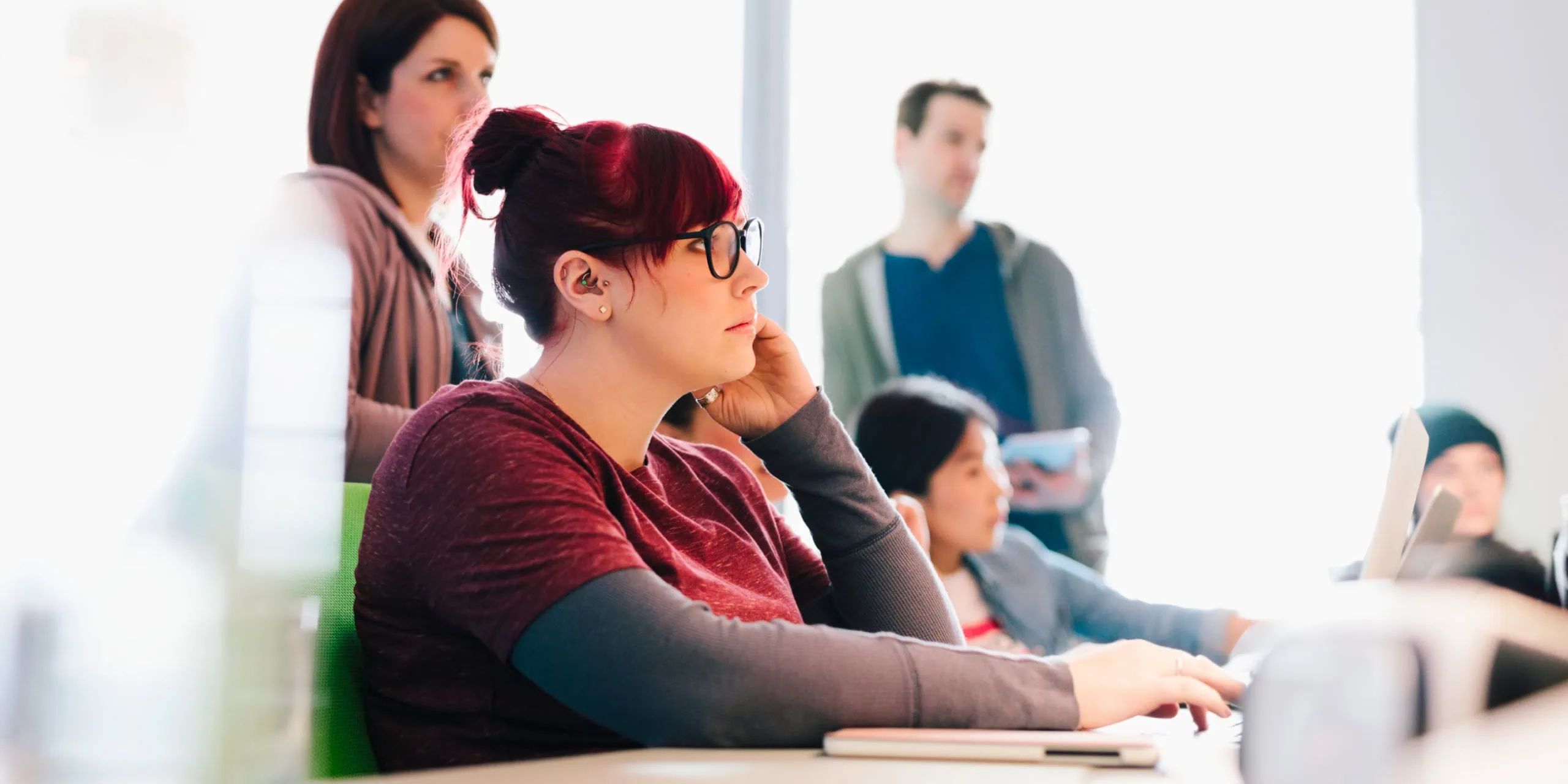 Team member working at a desk during a workshop, with colleagues in the background.