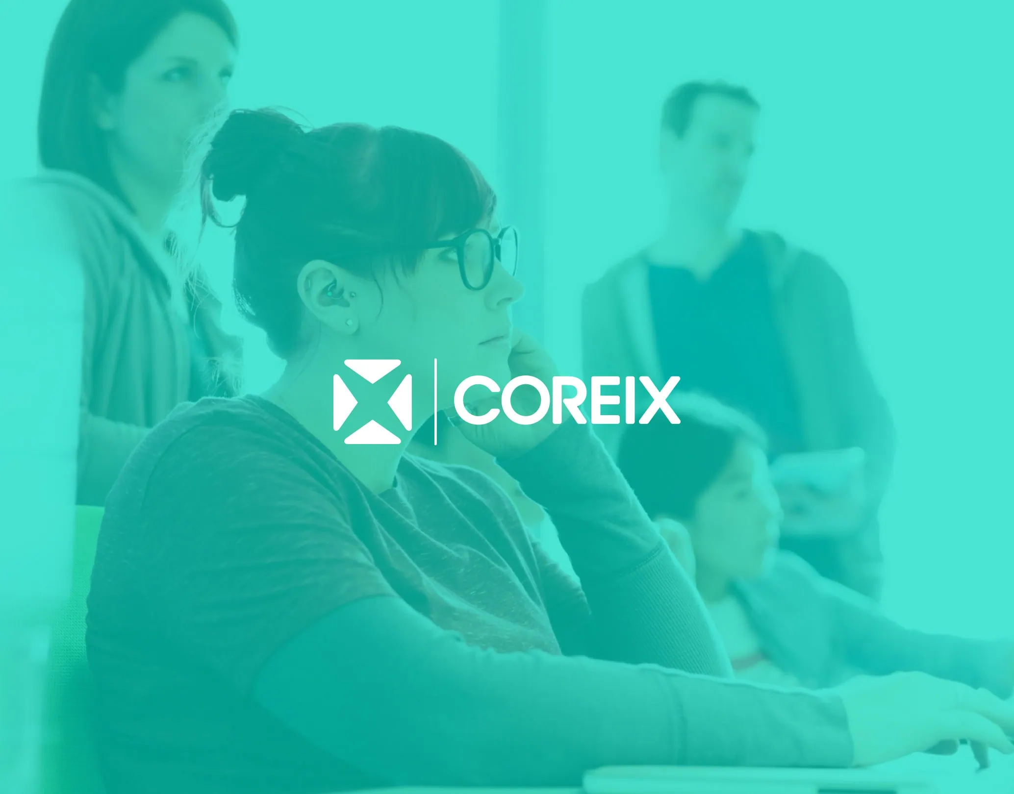 Coreix logo on a teal background over an image of a team member working at a desk during a workshop, with colleagues in the background.