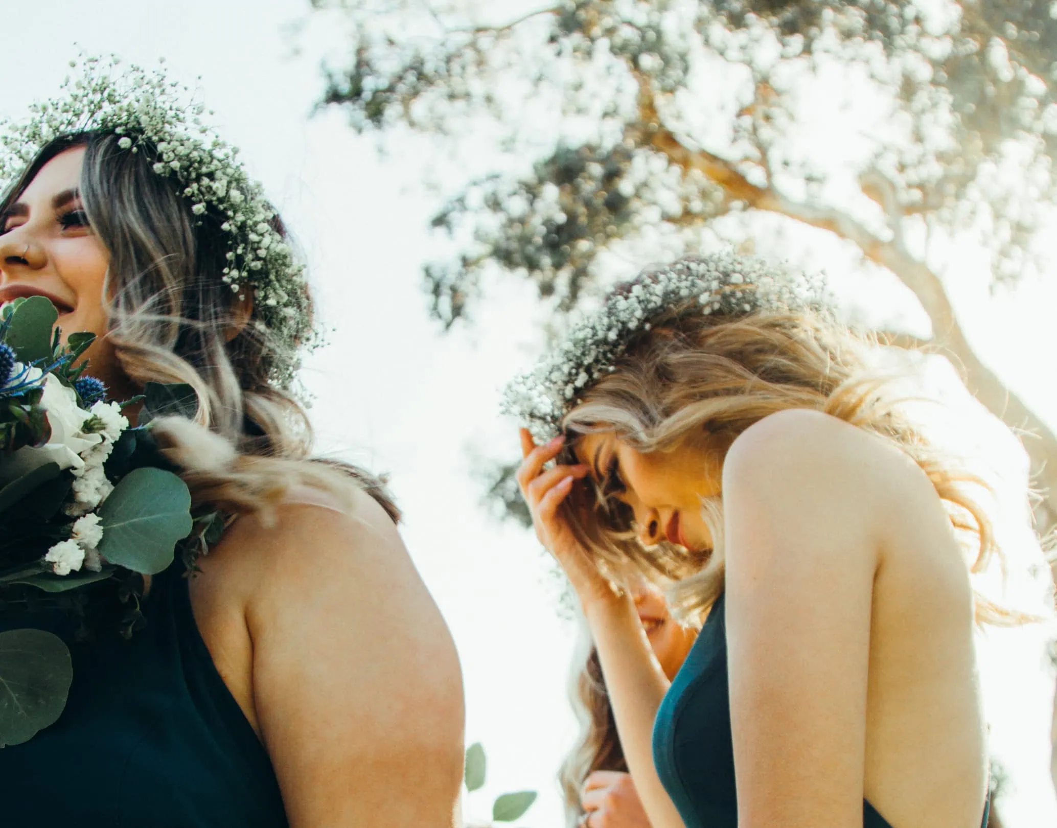 Two bridesmaids in floral crowns holding bouquets, photographed outdoors in bright sunlight