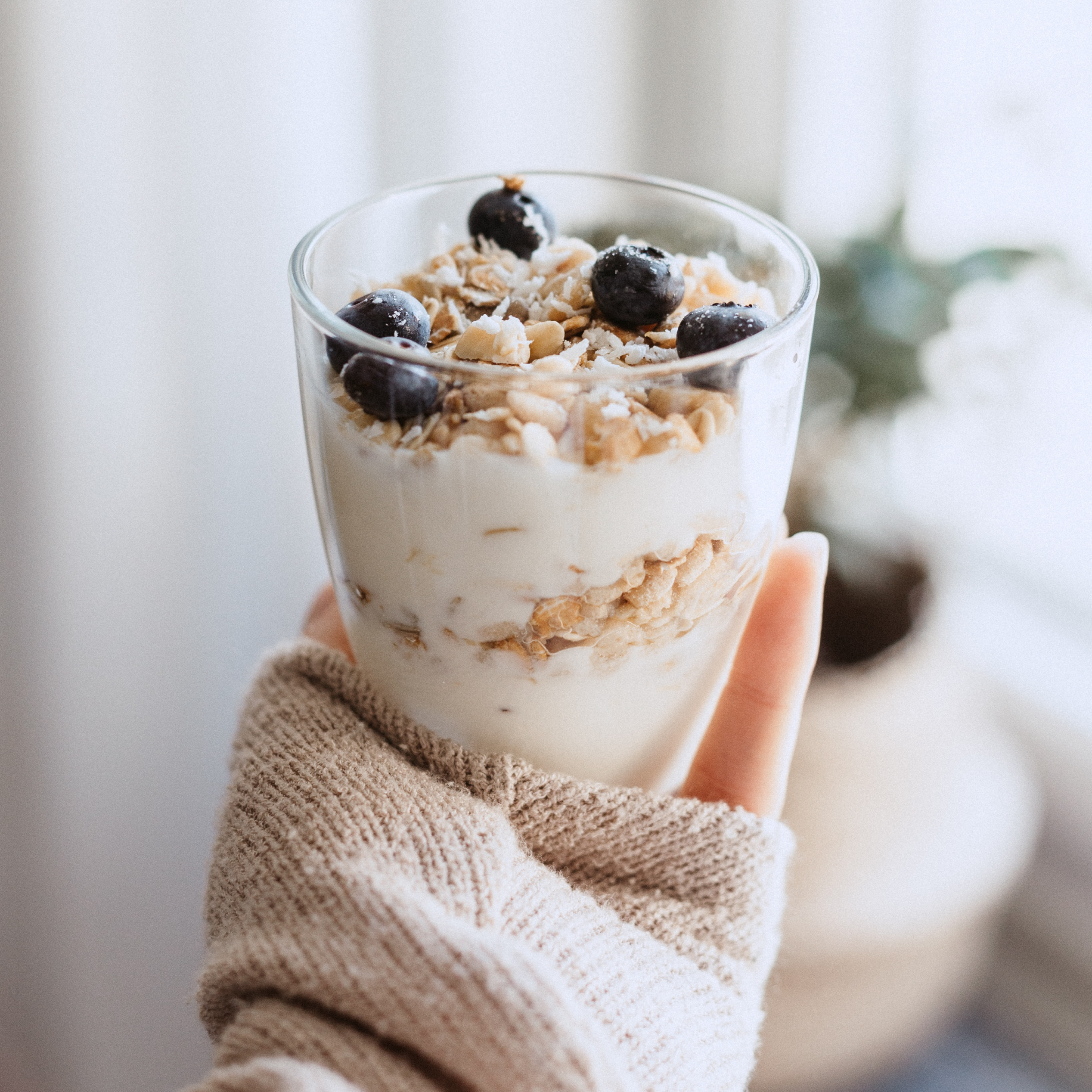 Hand holding a glass of yoghurt parfait topped with granola and blueberries