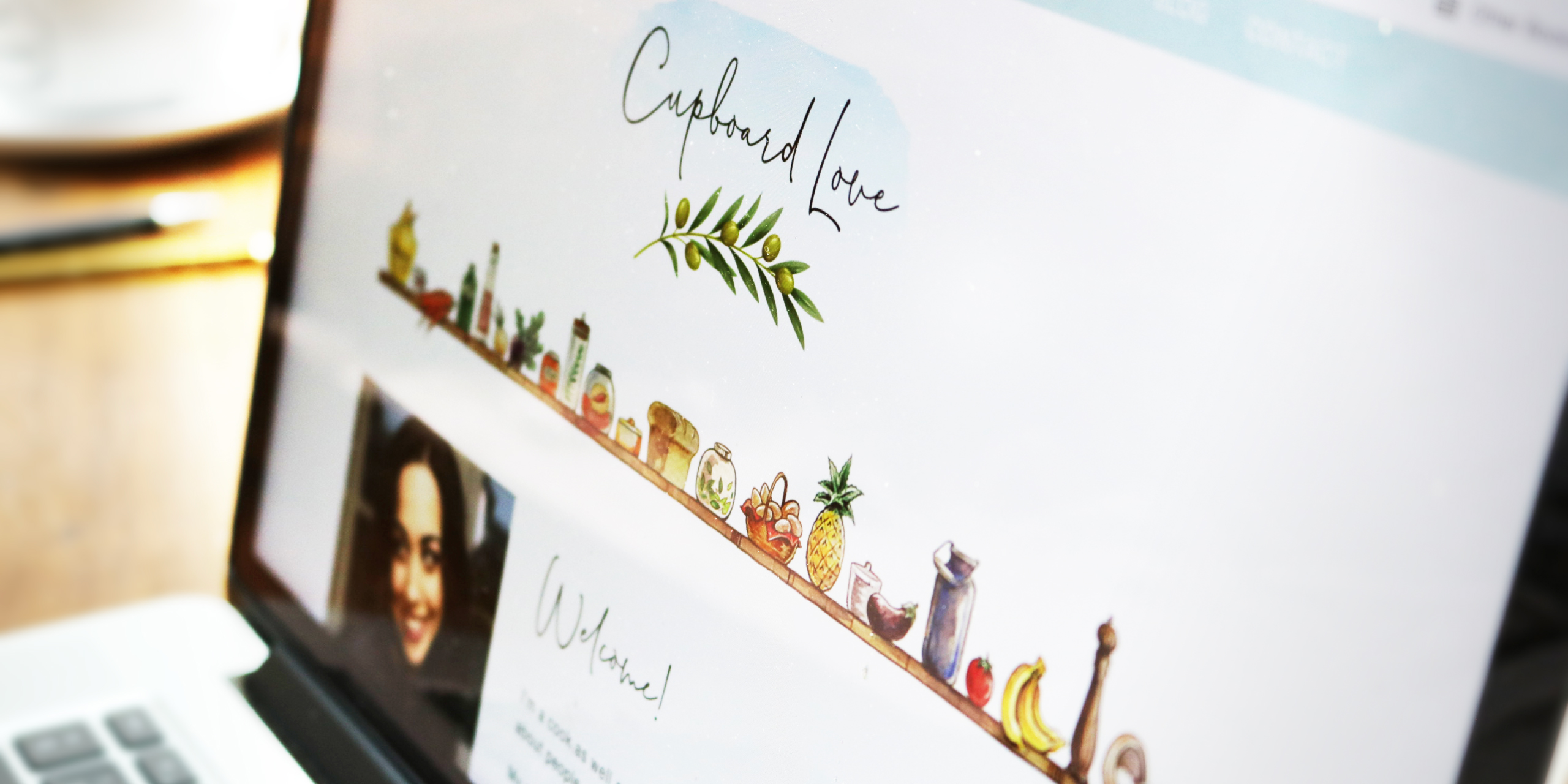 Close-up of the Cupboard Love website on a laptop showing the logo and illustrated food shelf graphic