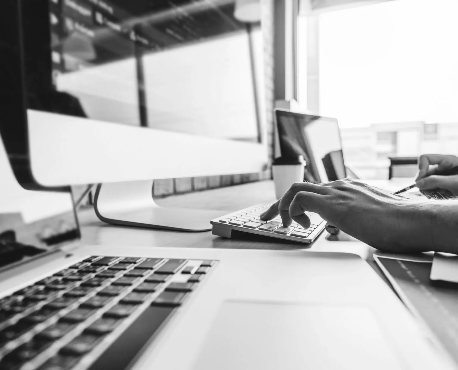 Close-up of persons hands operating a keyboard, with a screen in front