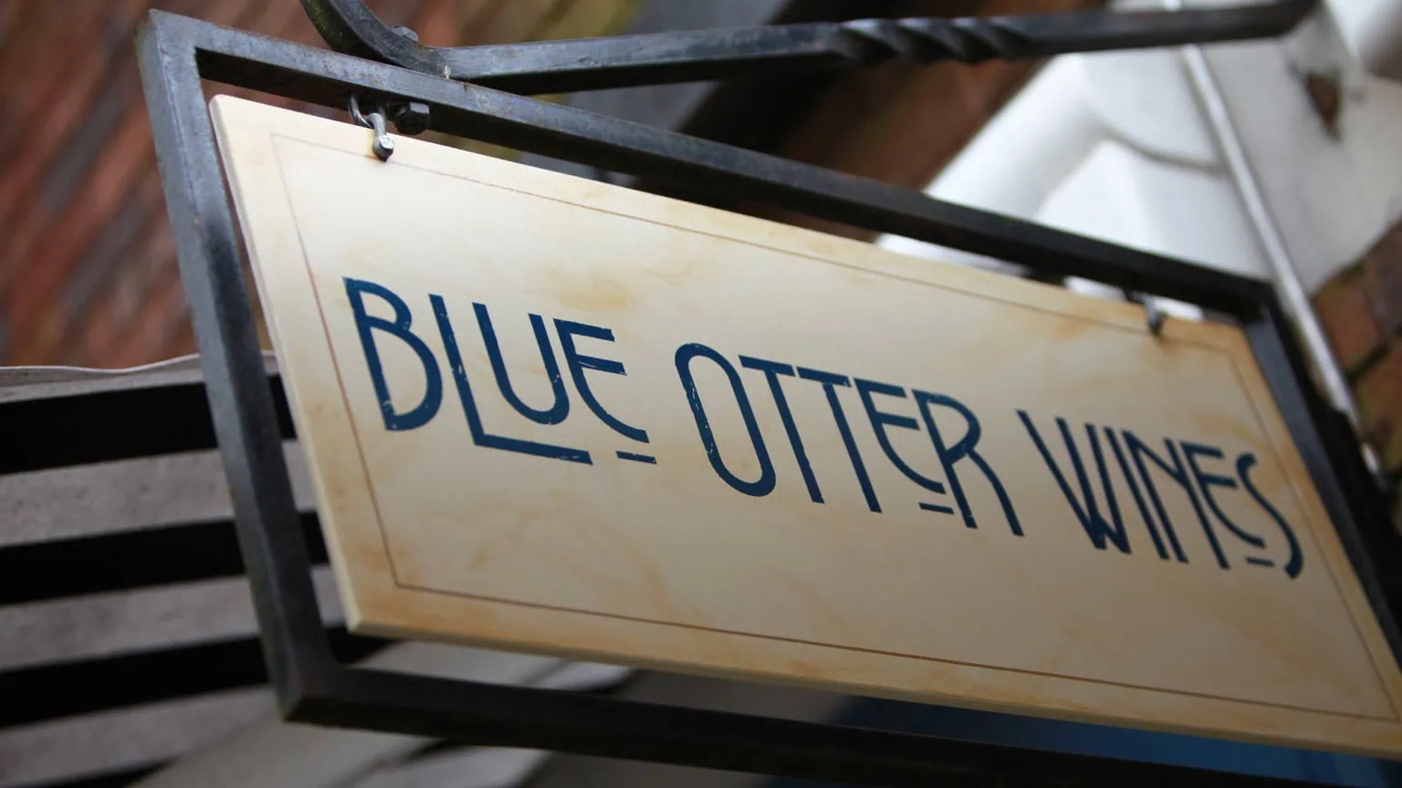 Hanging shop sign reading “Blue Otter Wines” in blue lettering on a cream background.