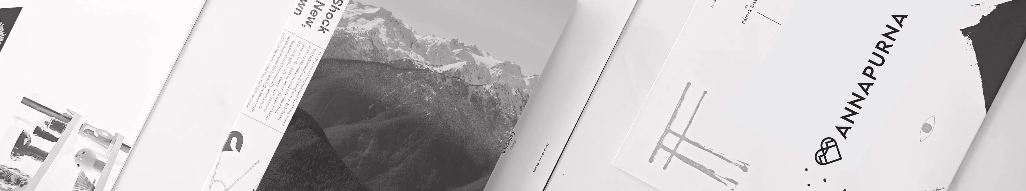 Flat lay of Annapurna branded print materials and magazine spreads featuring mountain imagery in monochrome.