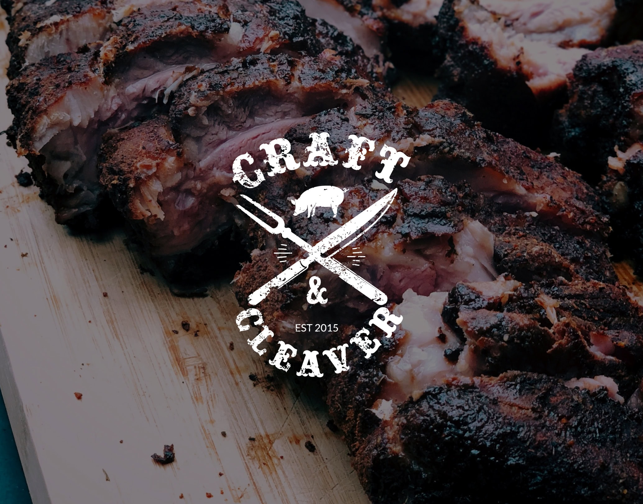 Rustic photograph of BBQ Ribs with Craft & Cleaver logo overlayed in white