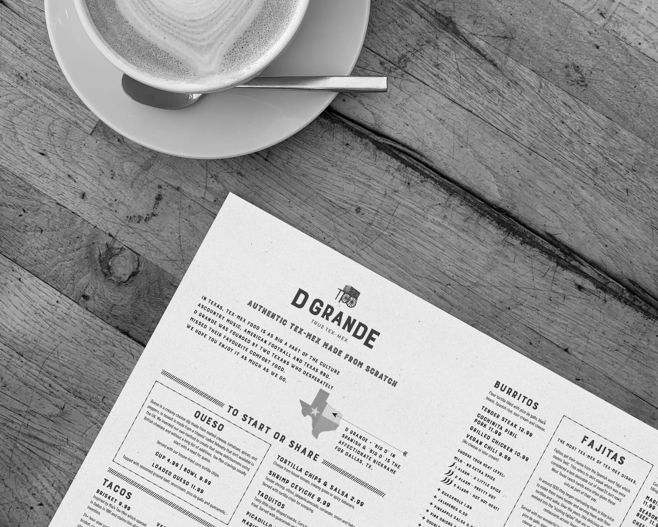 Coffee cup on a saucer beside a printed D Grande Tex-Mex menu on a rustic wooden table.